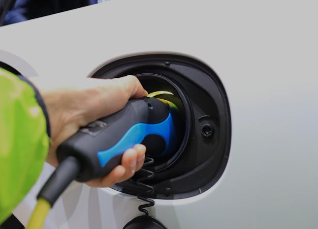 EV Car or Electric vehicle at charging station with the power cable supply plugged in on blurred nat...