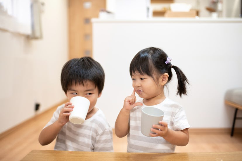 Asian children, brother and sister, drinking cup of milk in the room