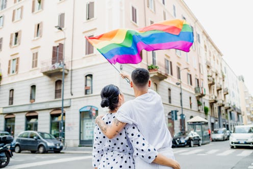 A couple waves a rainbow flag in a city. Here's what the rainbow represents on the gay pride flag.