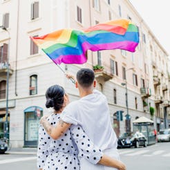 A couple waves a rainbow flag in a city. Here's what the rainbow represents on the gay pride flag.