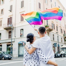 A couple waves a rainbow flag in a city. Here's what the rainbow represents on the gay pride flag.