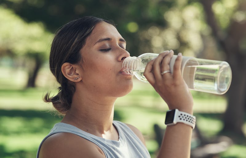 A person closes their eyes while drinking from a water bottle outside. Dry scooping pre-workout won't make it more effective, but it will make it more dangerous.