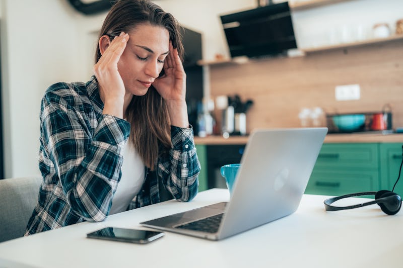 Woman at home with headache looking exhausted in front of laptop