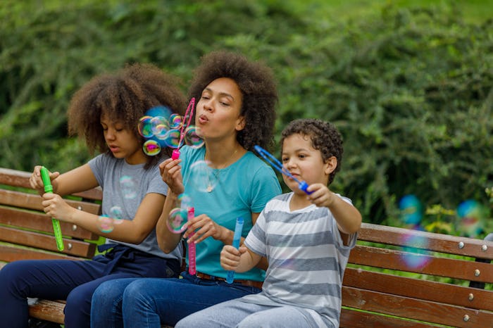 Mother of African-American Ethnicity is Sitting with Son and Daughter on a Bench in Public Park and ...
