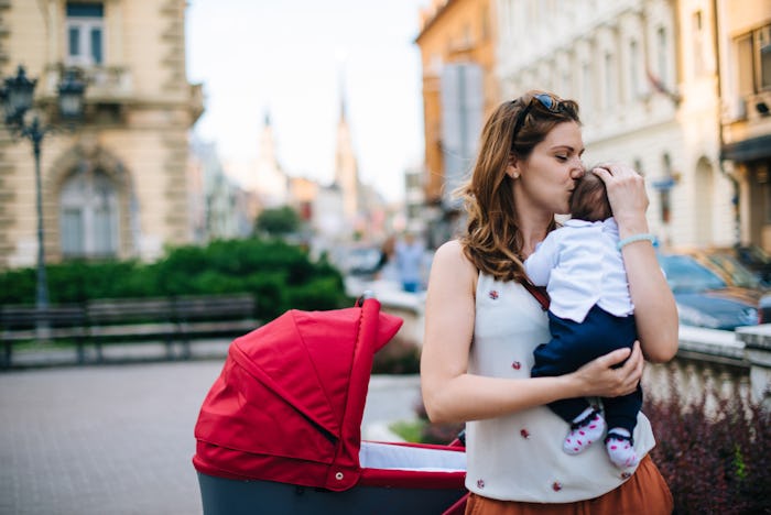 Millennial generation mother with baby in modern red pram walking in downtown on sunny summer day.