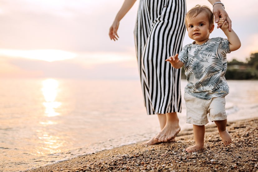 Mother and cute little baby boy walking at the beach, mother is unrecognisable