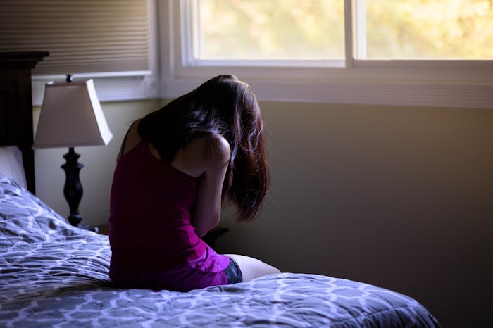 Back view of petite brunette sitting on bed. Bowed head in hands. Moody atmosphere, bad day, sadness...