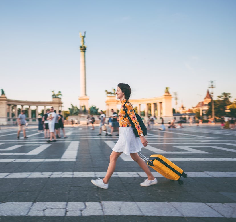 Young woman with suitcase just arriving in Budapest and walking through Hero’s square
