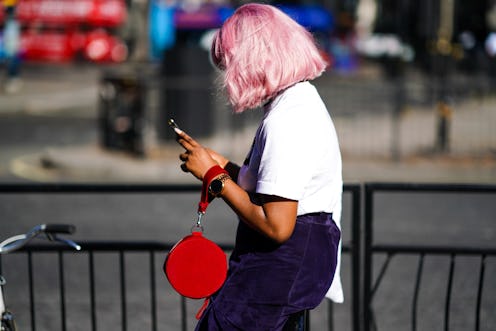 LONDON, ENGLAND - SEPTEMBER 14: A guest wears a white t-shirt, a navy blue skirt, a red circular bag...