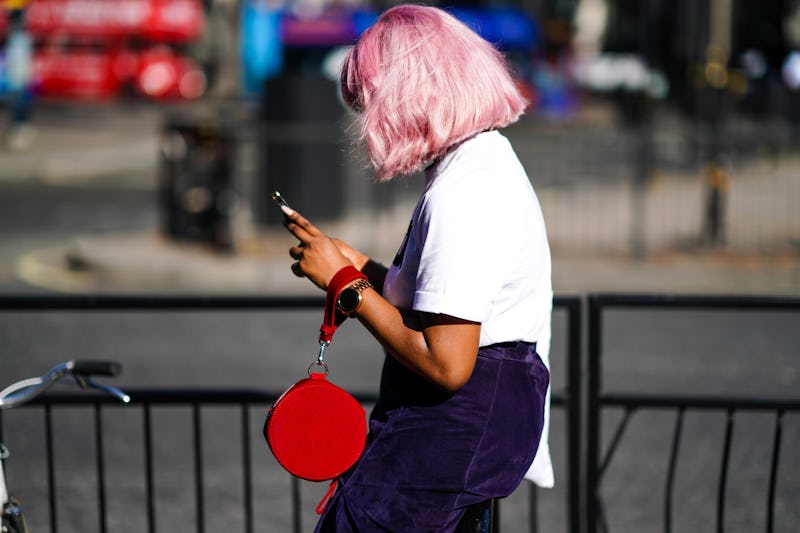 LONDON, ENGLAND - SEPTEMBER 14: A guest wears a white t-shirt, a navy blue skirt, a red circular bag...