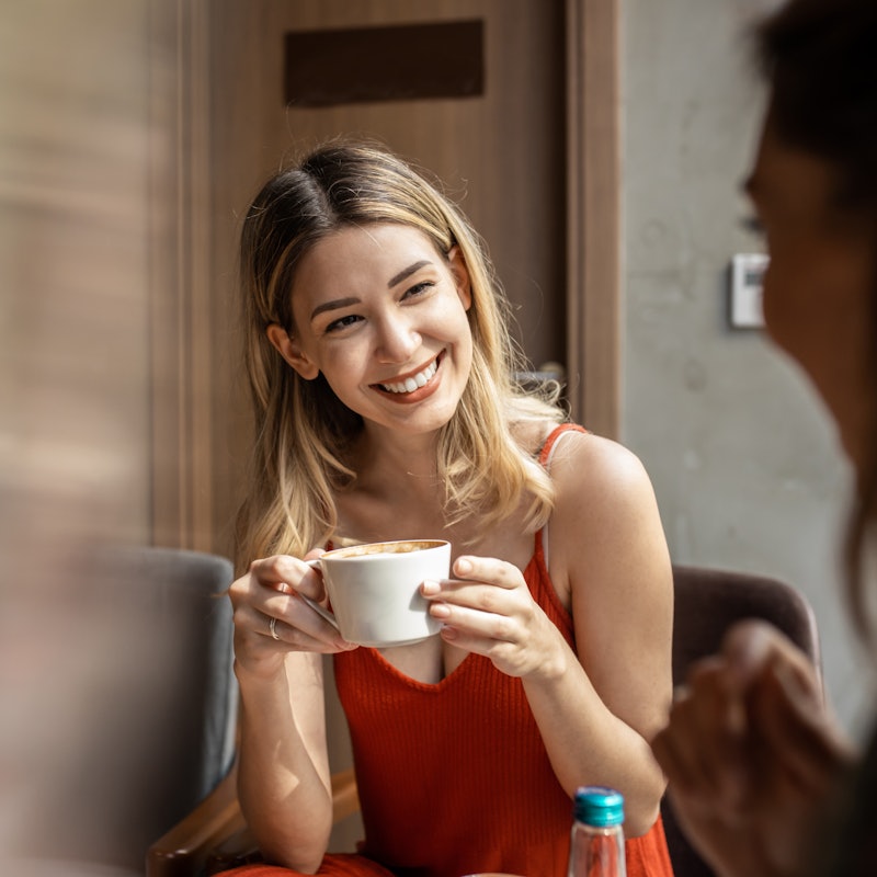 Beautiful happy women talking and laughing while drinking coffee together in coffee shop.