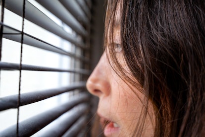 Head of a young woman afraid looking through venetian blinds on a window