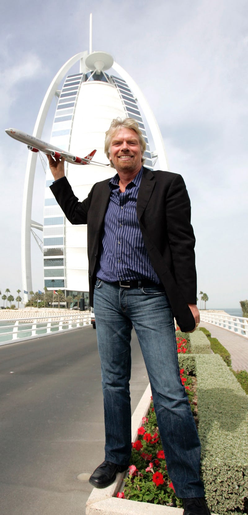 Sir Richard Branson holding a model Virgin airplane in front of Dubai's Burj Al-Arab hotel 