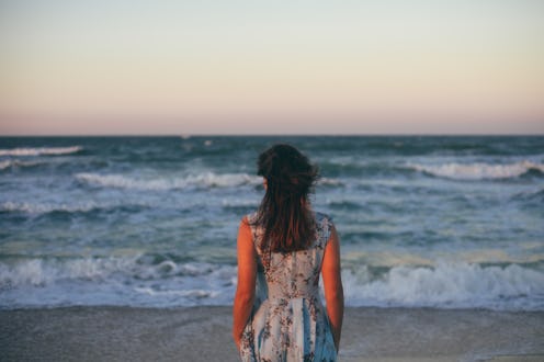 Portrait of young Caucasian woman in blue dress with dark hair outdoors by the sea on beach at sunse...