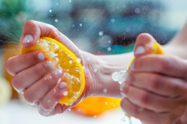 Woman squeezing the juice from a lemon. Some droplets of juice can be seen. Two halves of the lemon ...