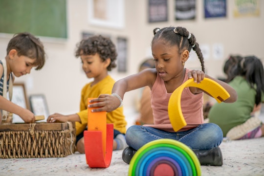 a little girl playing with a rainbow toy in the middle of a preschool classroom