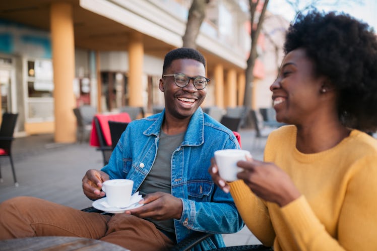 Happy smiling African American couple, sitting in a coffee shop, relaxing and enjoying their vacatio...