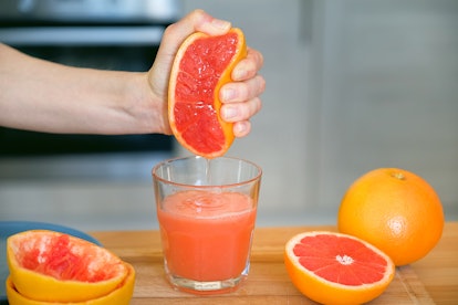 A girl or woman squeezes the juice from a red ripe grapefruit, squeezes the fruit with her hand. A g...