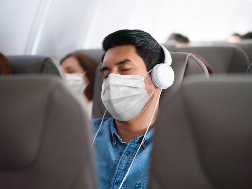 Portrait of a Latin American man traveling and sleeping on the plane wearing a facemask during the C...
