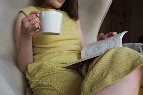 Woman reading a book with a cup of coffee in her hand.