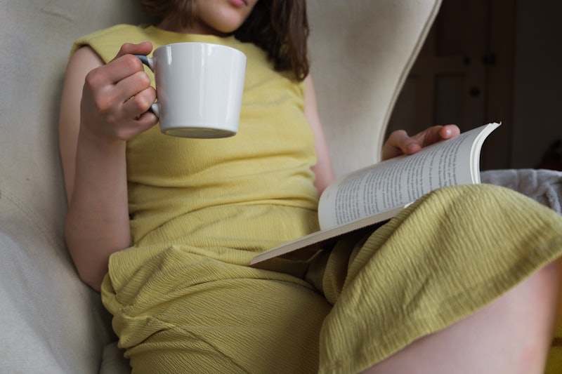 Woman reading a book with a cup of coffee in her hand.