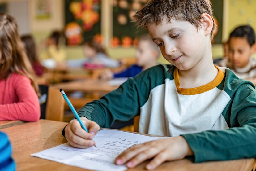 Schoolboy writing on a paper on his desk in the classroom.