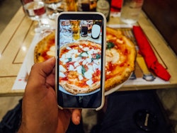 A man is taking a photo of his pizza in a restaurant in Naples, Italy. Searching Instagram locations...