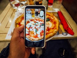 A man is taking a photo of his pizza in a restaurant in Naples, Italy. Searching Instagram locations can help you find new places to eat or sus out the vibe at a public spot.