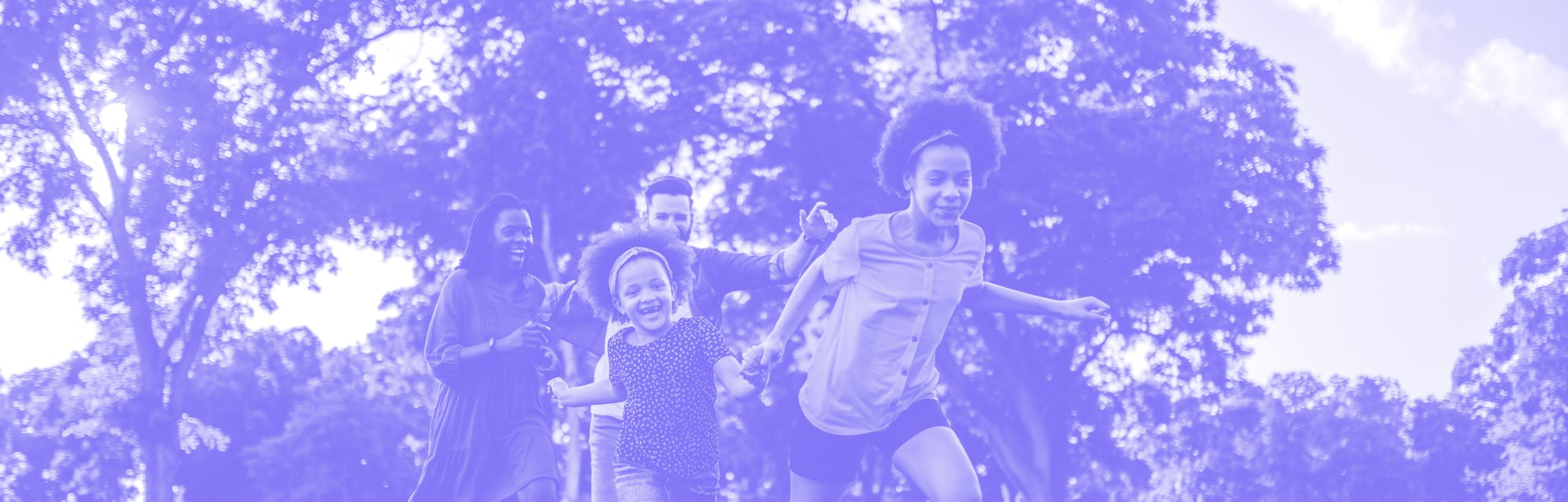 Multi-ethnic family is running outside in a grassy field - they are laughing while chasing each othe...