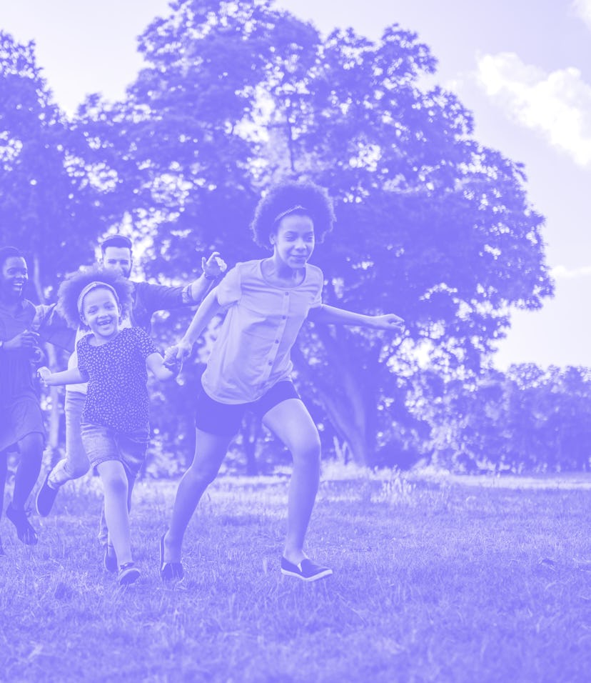 Multi-ethnic family is running outside in a grassy field - they are laughing while chasing each othe...