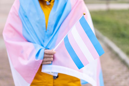 Transgender woman covered with the transgender flag and holding a flag in the hand for defending her...