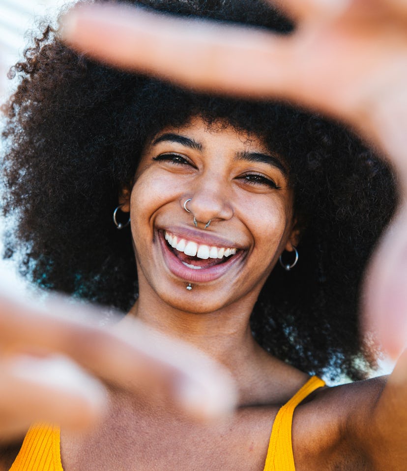 Smiling young woman making a camera sign with her fingers while learning the emotional meaning of th...