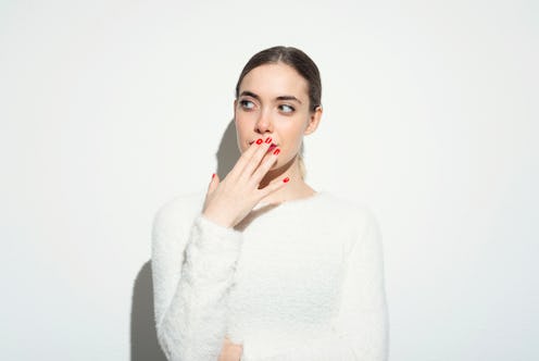 Portrait of beautiful young woman holding hand in front of her mouth against white background.Studio...