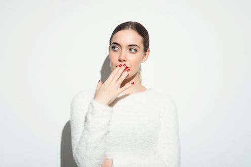 Portrait of beautiful young woman holding hand in front of her mouth against white background.Studio...