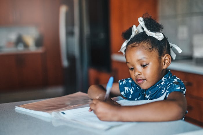 little girl writing in notebook at the kitchen table