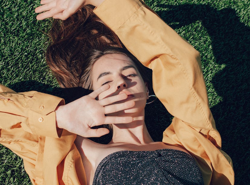 Young woman laying in the grass while reading her new moon in Leo horoscope.