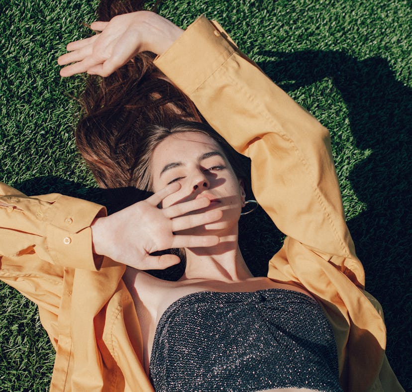 Young woman laying in the grass while reading her new moon in Leo horoscope.