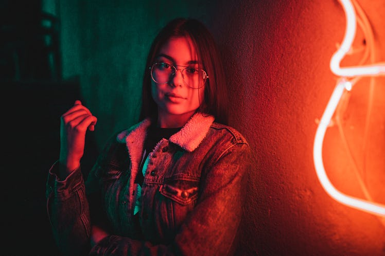 Portrait of beautiful casual dressed teenage girl standing next to neon light at night