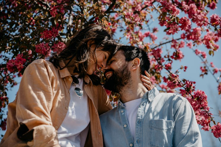 Cute young adult couple snuggling noses while enjoying under the tree, on a beautiful sunny day, wit...