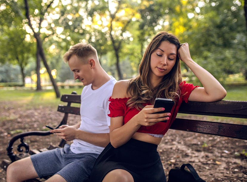 Young girl and her boyfriend with smartphones ignoring each other during date at park
