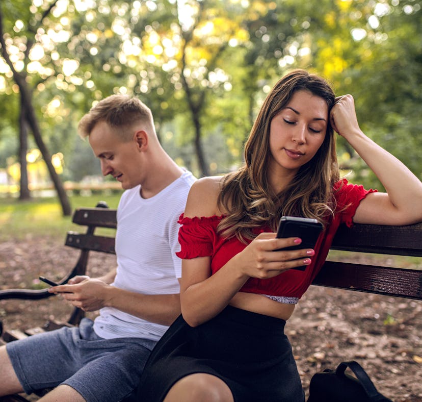 Young girl and her boyfriend with smartphones ignoring each other during date at park