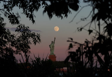 JERSEY CITY, NJ - JUNE 23: An almost full moon rises above the Statue of Liberty as the sun sets in ...