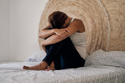 Unrecognizable abused woman lying on her bed scared and crying with her head between her knees. Conc...