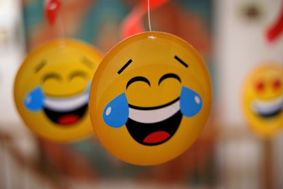 Close-up of handing round paper emoticon. Yellow laughing face with big blue tears at eyes. Selectiv...
