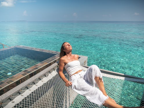 30's woman relaxing on hammock over sea in luxury private villa in the Maldives Islands