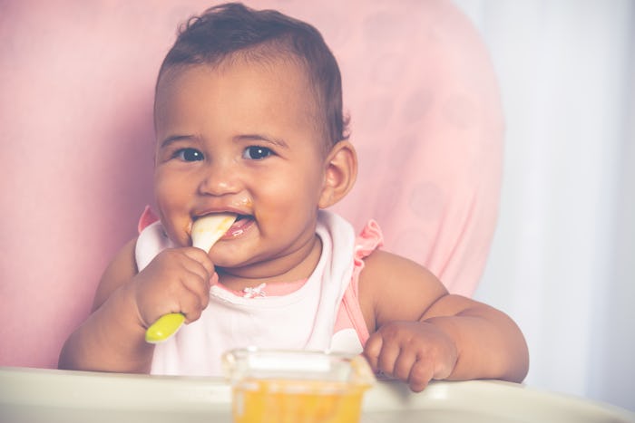 Cute baby child eating pureed mango with a teaspoon.