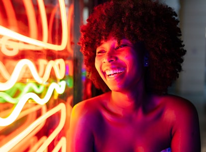 Young woman smiling and laughing next to neon sign on Friday the 13th 2021.