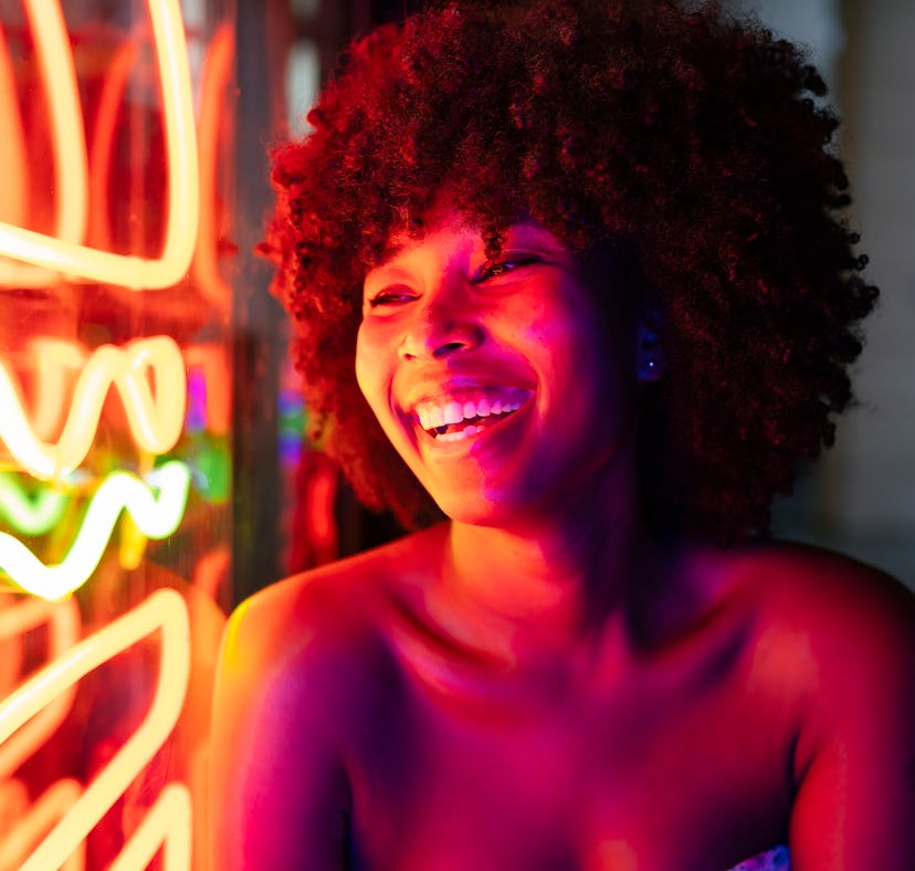 Young woman smiling and laughing next to neon sign on Friday the 13th 2021.