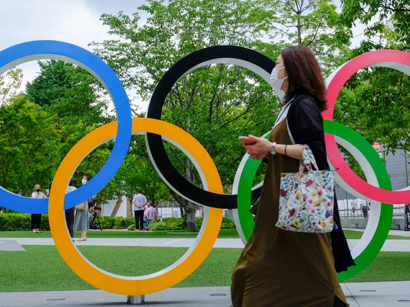 TOKYO, JAPAN - 2021/07/15: A woman wearing a face mask walks past Olympic Rings near the National St...
