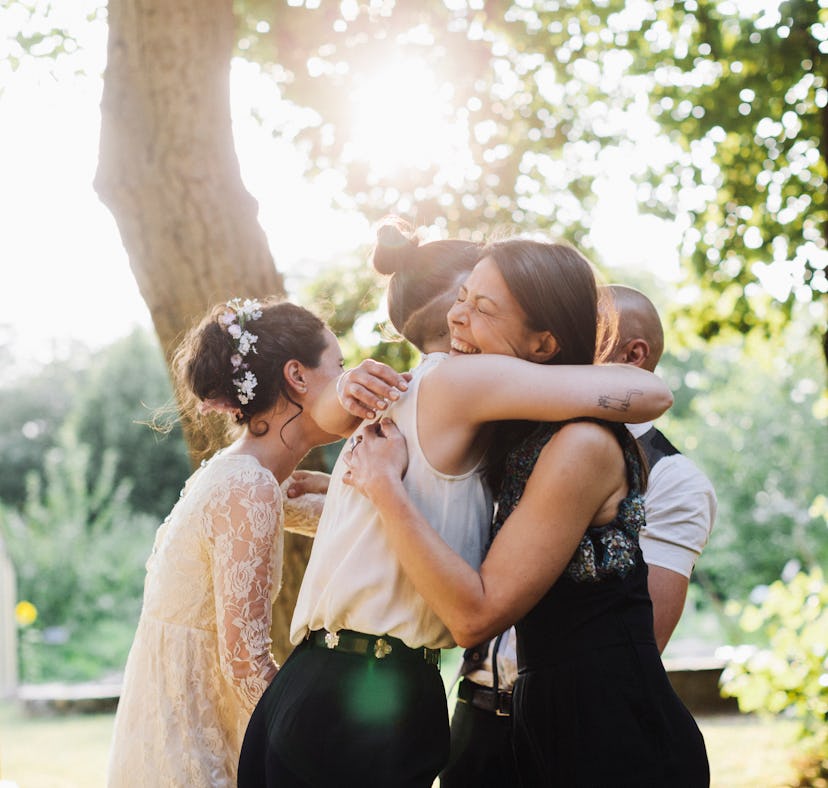 Young woman attending her coworker's wedding, hugging bride.